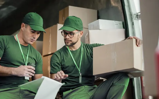 Two couriers checking a delivery list beside parcels in a van